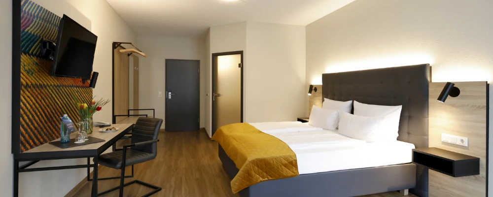 Modern eingerichtetes Doppelzimmer mit großem Bett, Schreibtisch, Wandfernseher und Holzboden