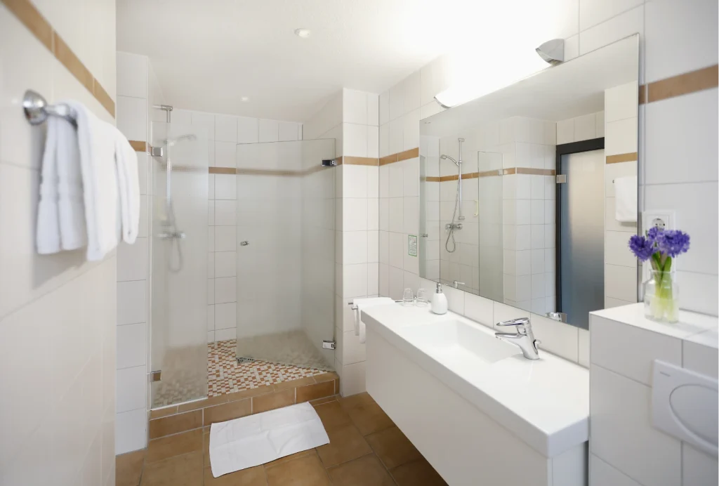 Helles Badezimmer mit großer Spiegelwand, Doppelwaschbecken, begehbarer Dusche mit Glasabtrennung und Handtüchern an der Wand
