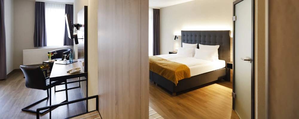Doppelzimmer mit großem Bett, Holzboden und Balkon mit Blick auf helle Vorhänge