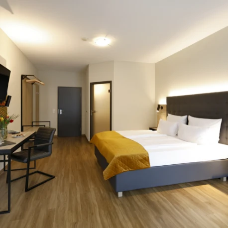 Modern eingerichtetes Hotelzimmer mit Doppelbett, Schreibtisch und Stuhl auf Holzboden