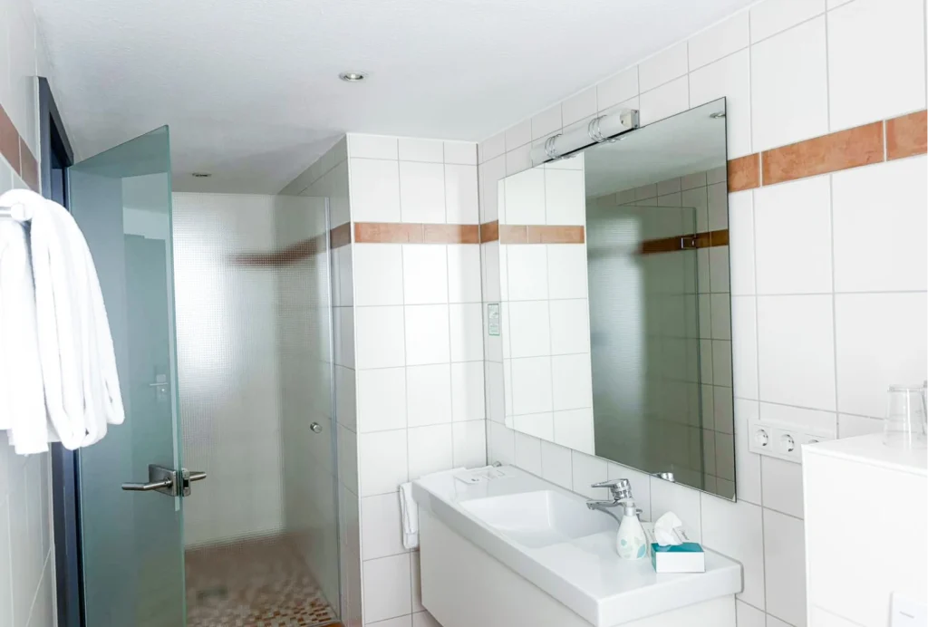Badezimmer mit großem Spiegel, Waschbecken, Handtüchern und Glastür zur Dusche